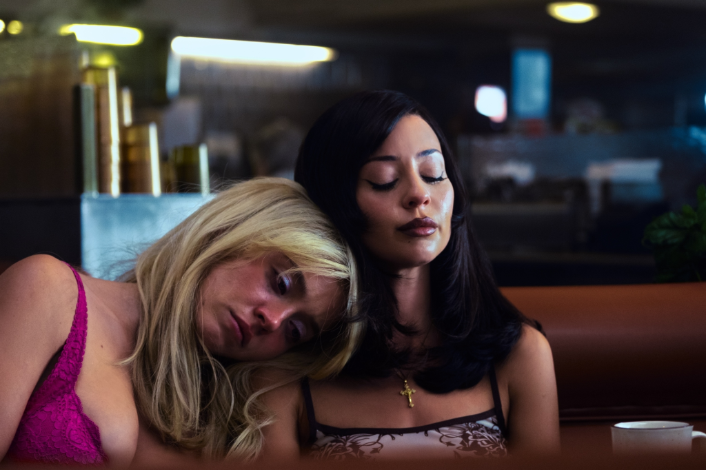 Two women leaning on each other with their eyes closed in a diner.