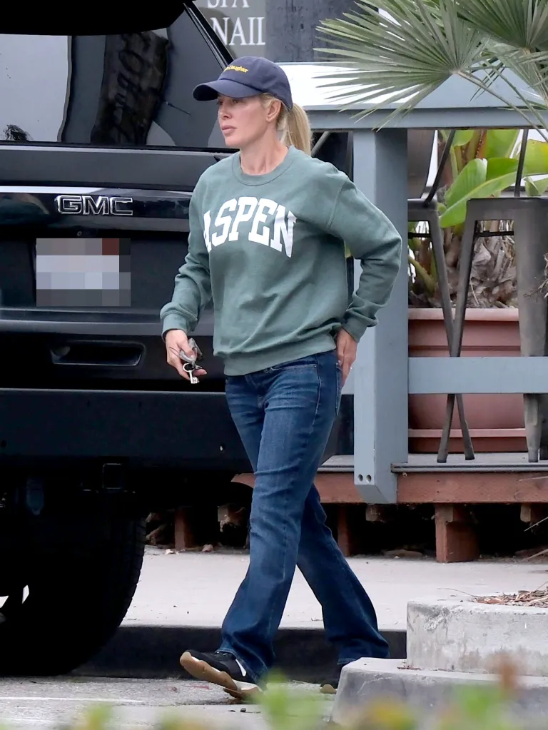 Heidi Pratt, wearing a green "ASPEN" sweatshirt, jeans, and a navy baseball cap, walks across a parking lot while running errands in Carpinteria, CA.