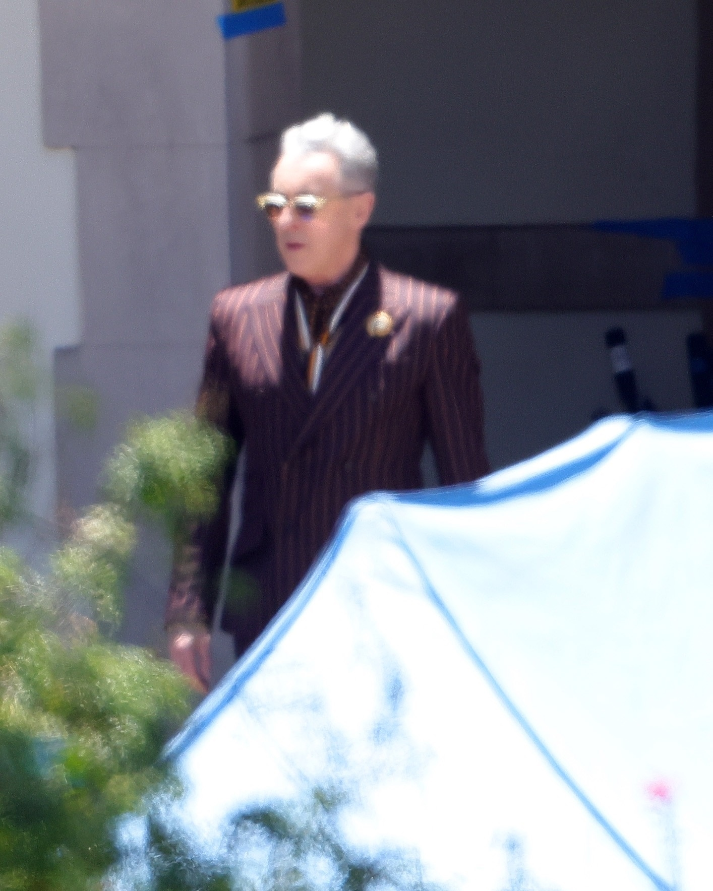 Alan Cumming as Sandy Frink in a purple striped suit and sunglasses.