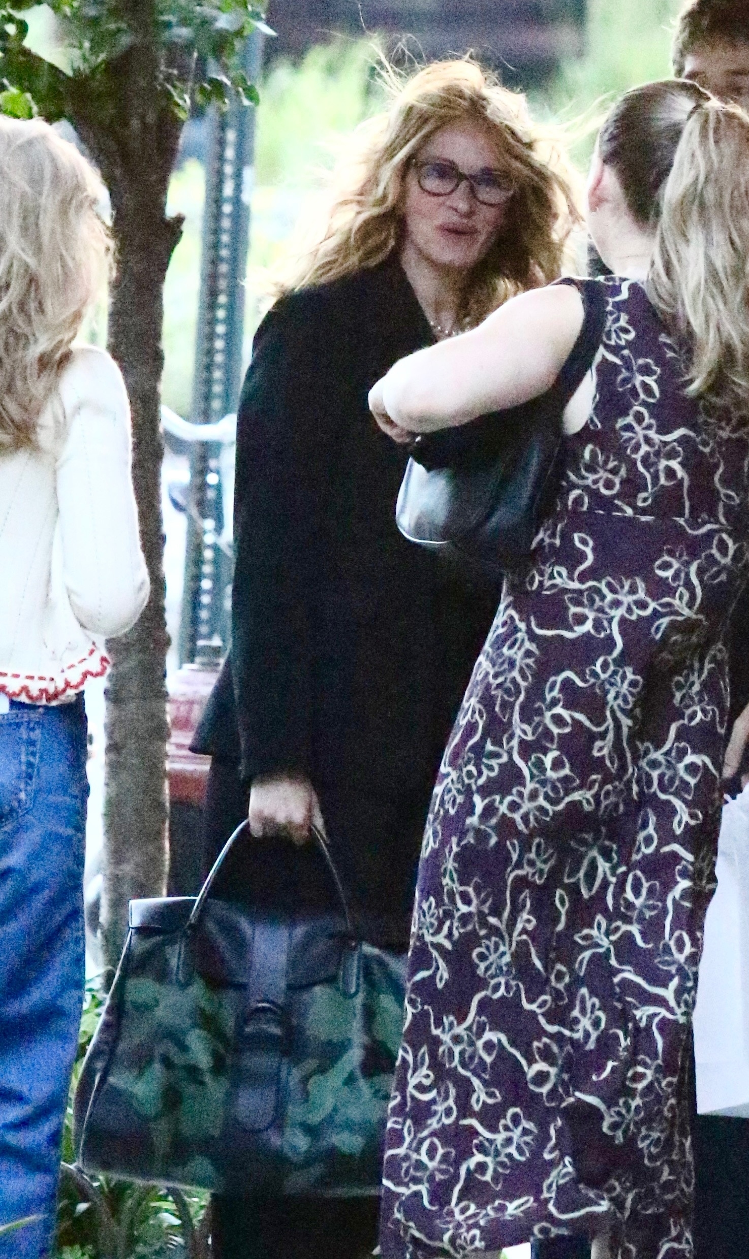 Julia Roberts wearing glasses and a dark suit, holding a camo-print bag, smiling at her daughter Hazel.