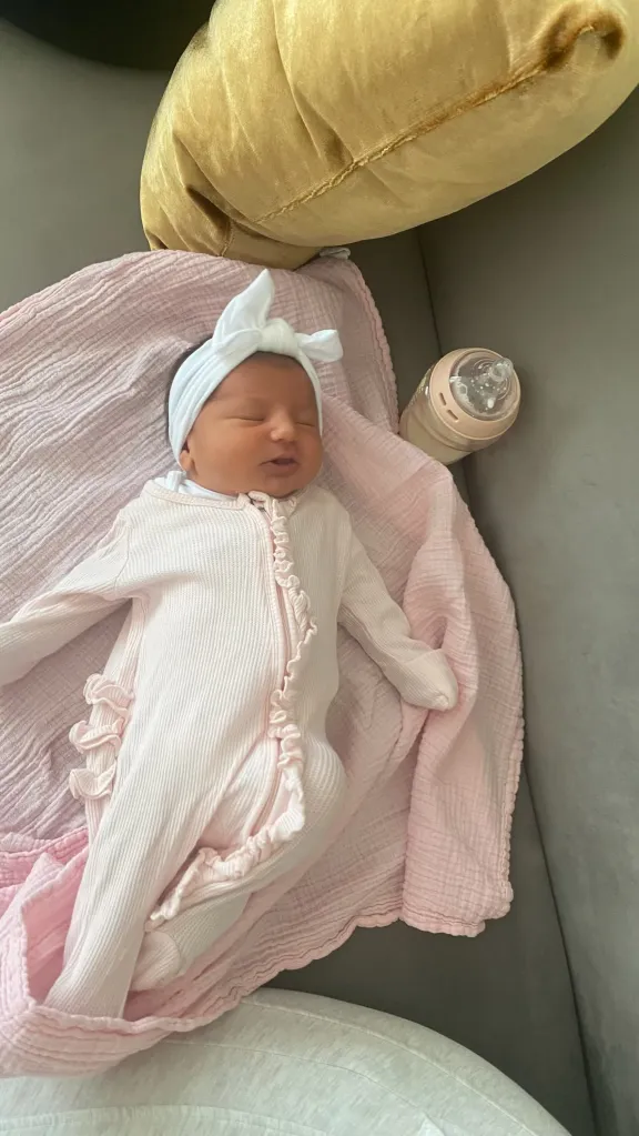 Baby Ella sleeping in a pink outfit with a bottle next to her.