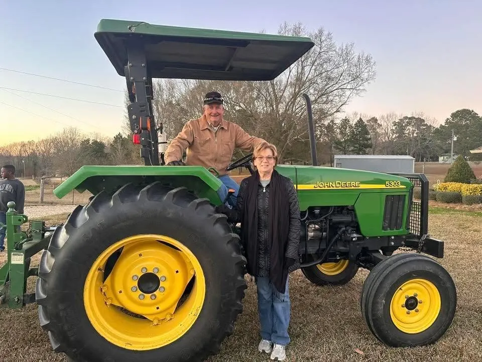 Billy Blair on a John Deere tractor with his wife, Virginia Carol Blair, standing beside it.
