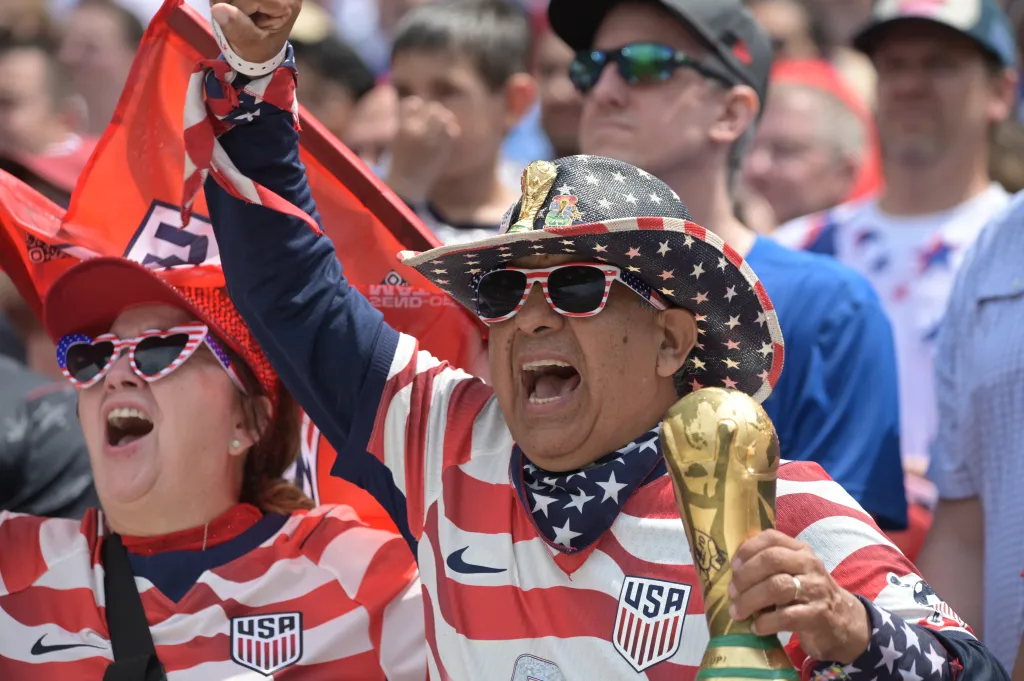 Fans wearing USA soccer jerseys cheer at an international friendly match.