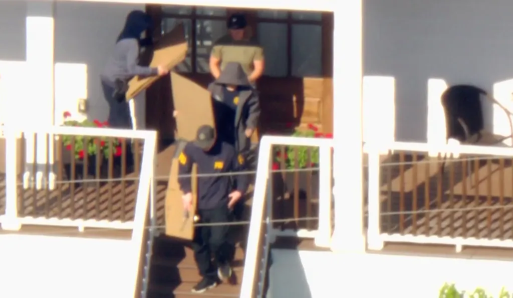 Federal officers raiding a home and carrying boxes.