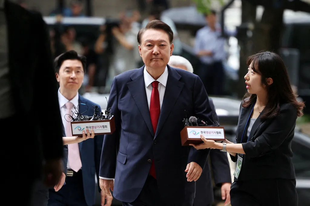 Former South Korean President Yoon Suk Yeol walks through a crowd as two people hold boxes containing microphones with the text "Korean Video Journalists Association".