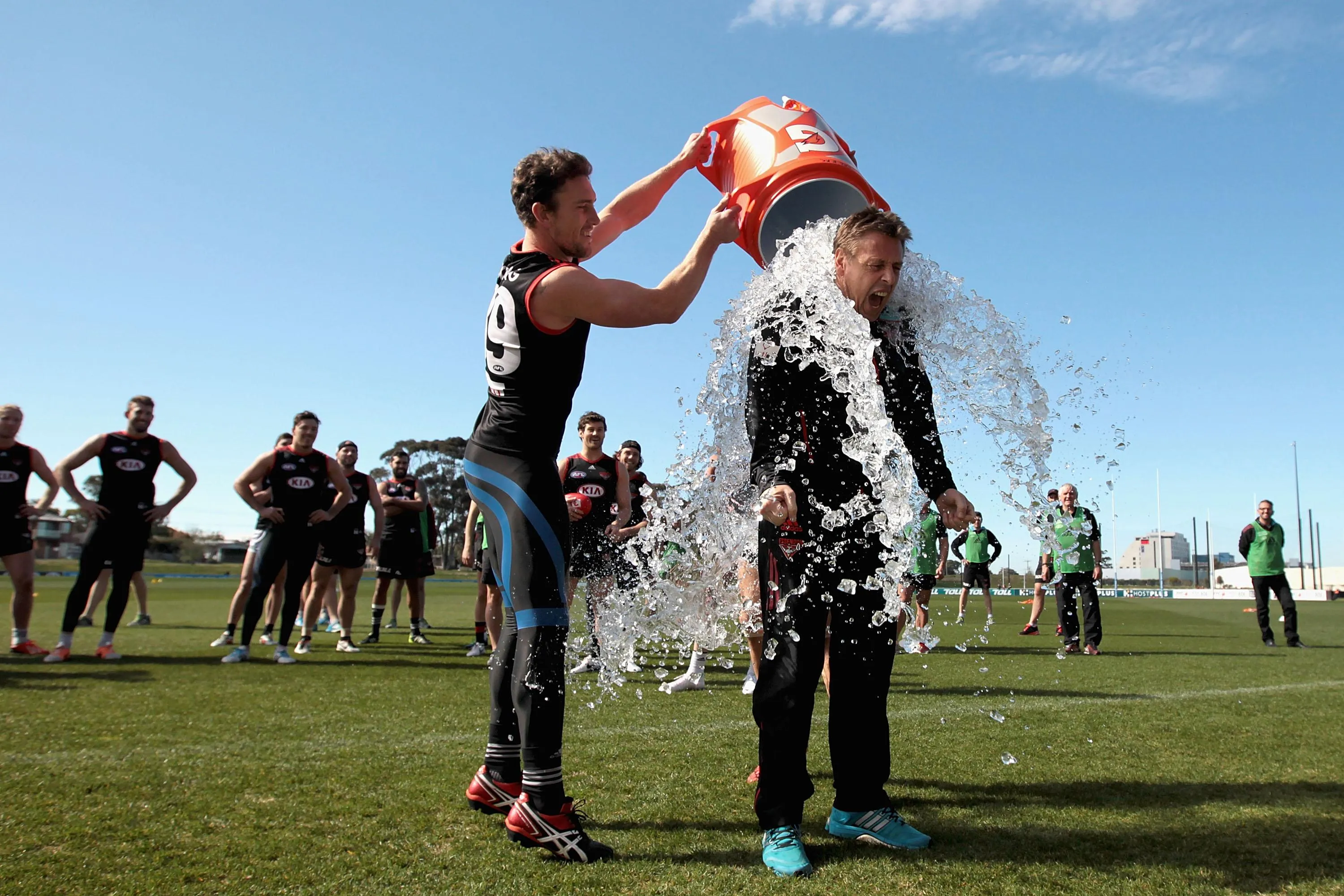 A man pours a bucket of ice water over another man while standing on a sports field A man pours a bucket of ice water over another man while standing on a sports field