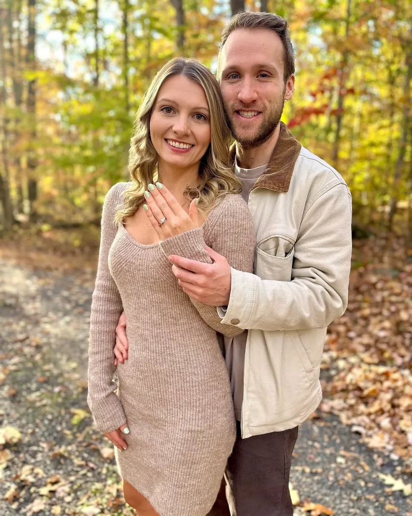 A man and a woman stand together outdoors, the woman showing off an engagement ring.