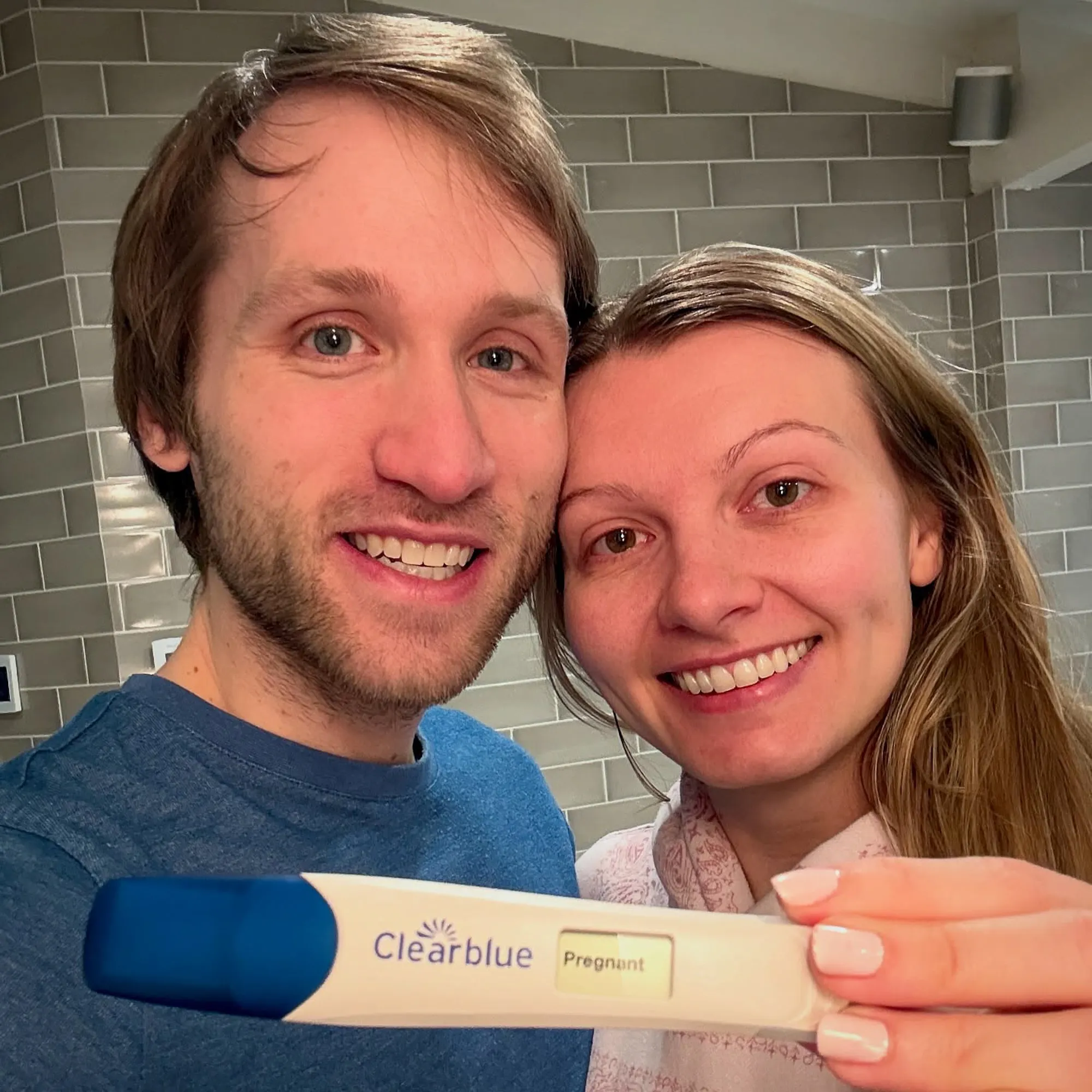 Jesse Ridgway and his wife smile while holding a Clearblue pregnancy test with the word "Pregnant" displayed.
