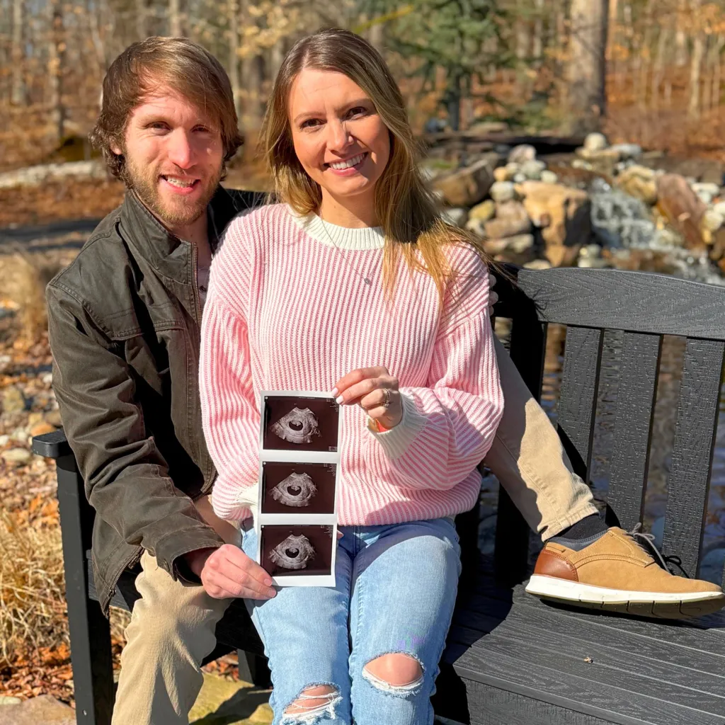 A man and a woman sitting on a bench, holding up sonogram images.