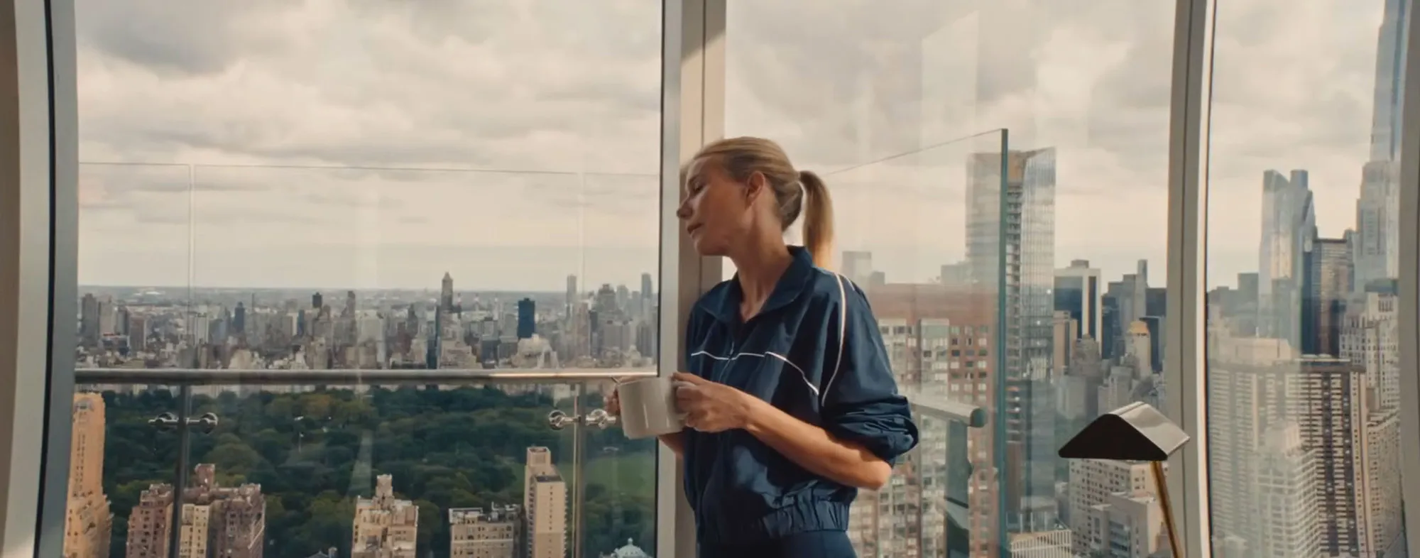 Gwyneth Paltrow holding a mug and looking at the cityscape view from a luxury condo balcony.