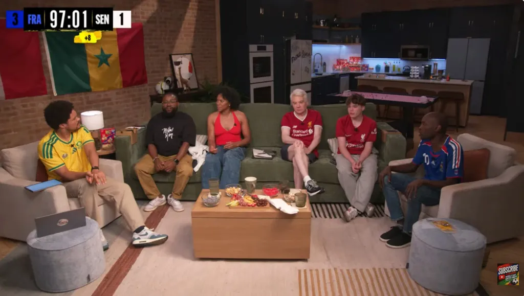 Six people watching a soccer game, with two wearing Liverpool shirts, two wearing jerseys from France, and one wearing a Senegalese jersey.