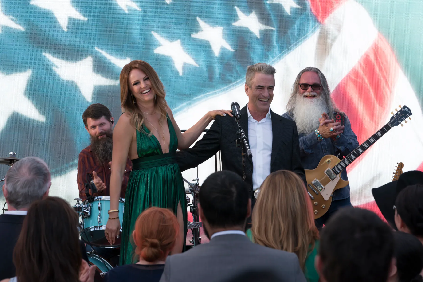 Margo Banks (Malin Åkerman) in a green dress and Jed Banks (Dermot Mulroney) standing next to a band in front of an American flag.