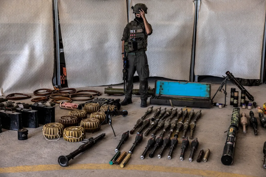 IDF Major G stands next to a display of confiscated Hamas weapons, including rockets, missiles, mines, and grenades.