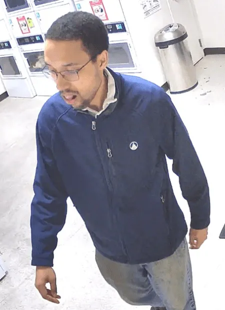 A man in a navy blue jacket and glasses looking down and to the left.