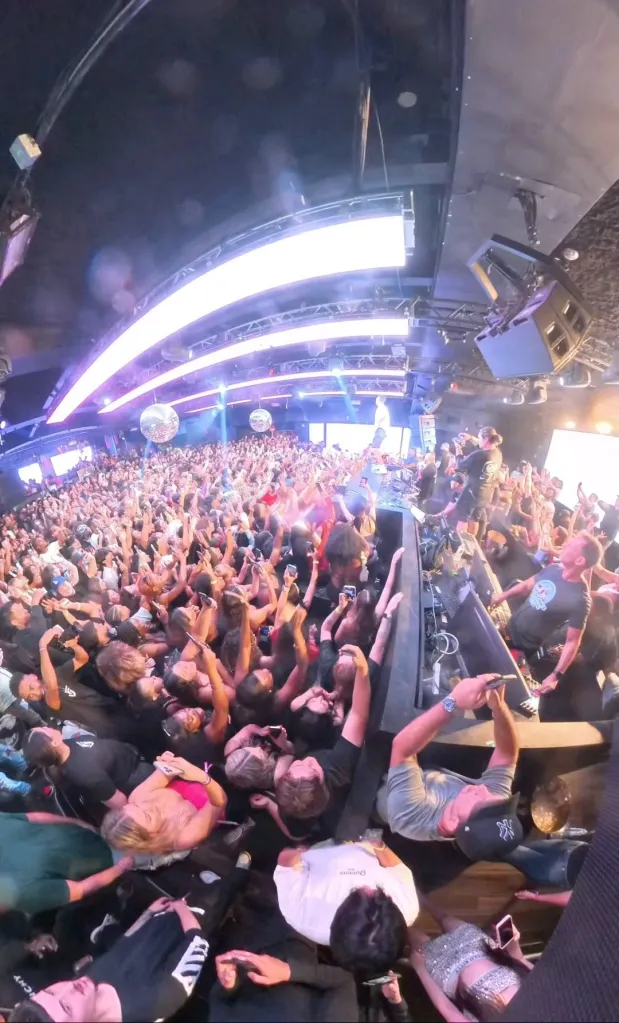 A high-angle photo shows a crowded club with many people dancing and holding up their phones.