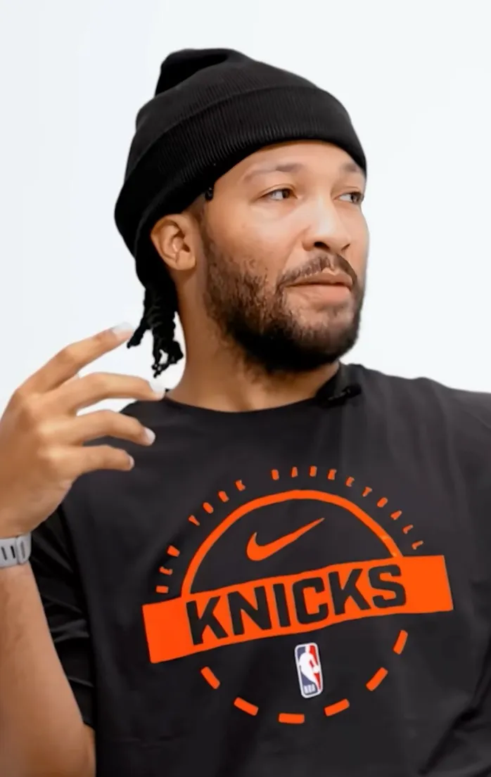 Jalen Brunson in a black beanie and Knicks t-shirt, gesturing with his hand.