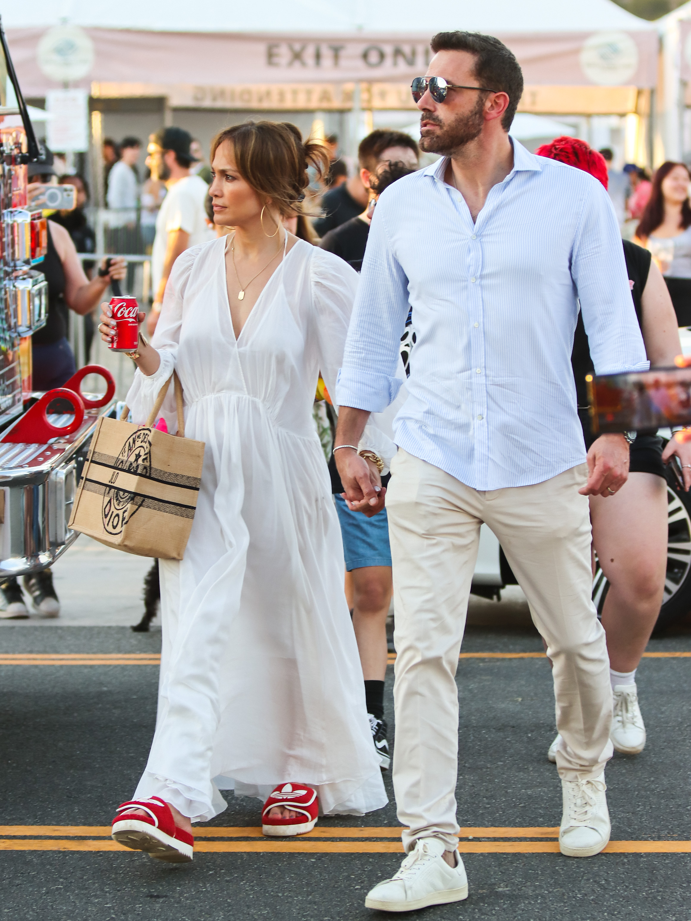 Jennifer Lopez in a white dress and Ben Affleck in a light blue shirt holding hands.