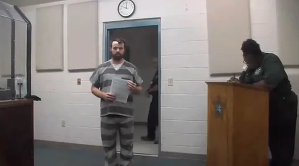 Joseph Duggar standing in a courtroom, holding papers, while a bailiff stands at a podium.