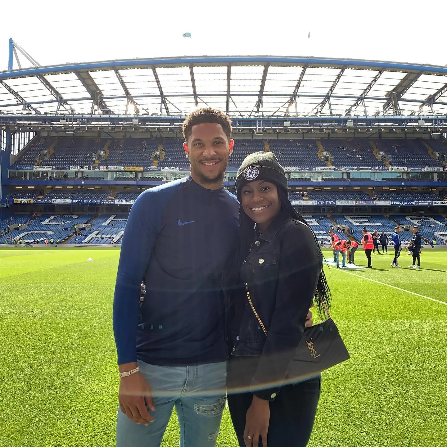 Josh Hart and Shannon standing on a soccer field in front of stadium seating.