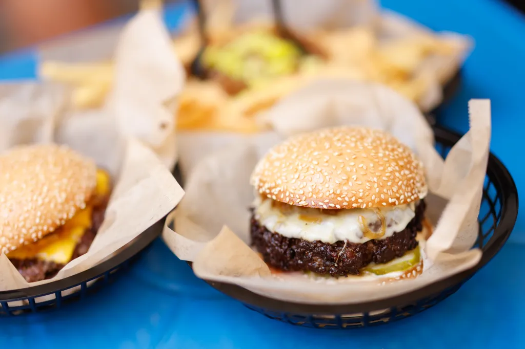 Cheeseburgers with fries in the background from Amboy Quality Meats & Delicious Burgers.
