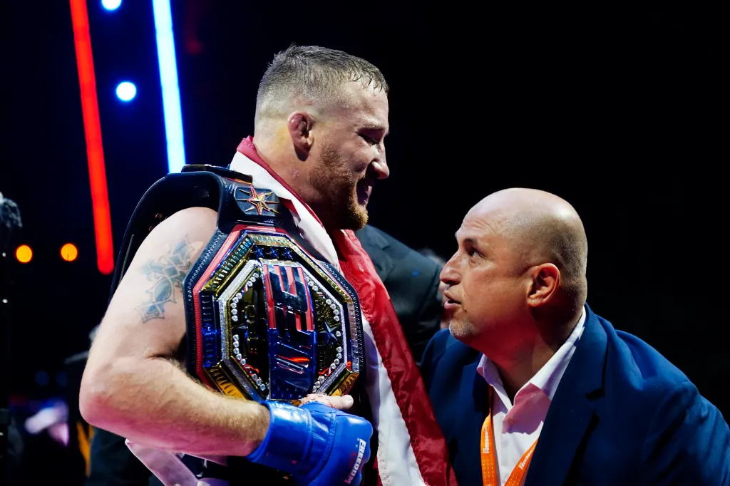 Justin Gaethje with his UFC Lightweight title belt, talking to a man in a suit.