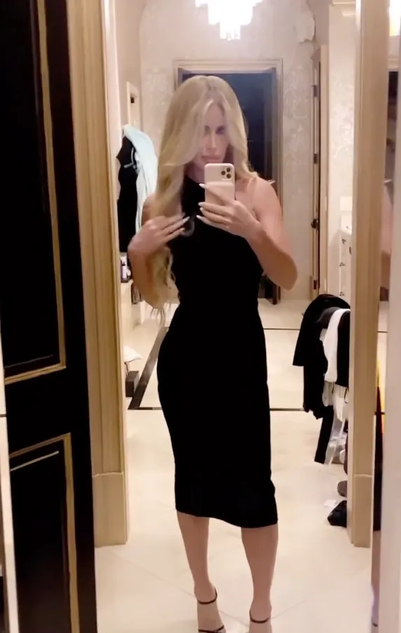 Kim Zolciak in a black dress, posing in a mirror selfie.