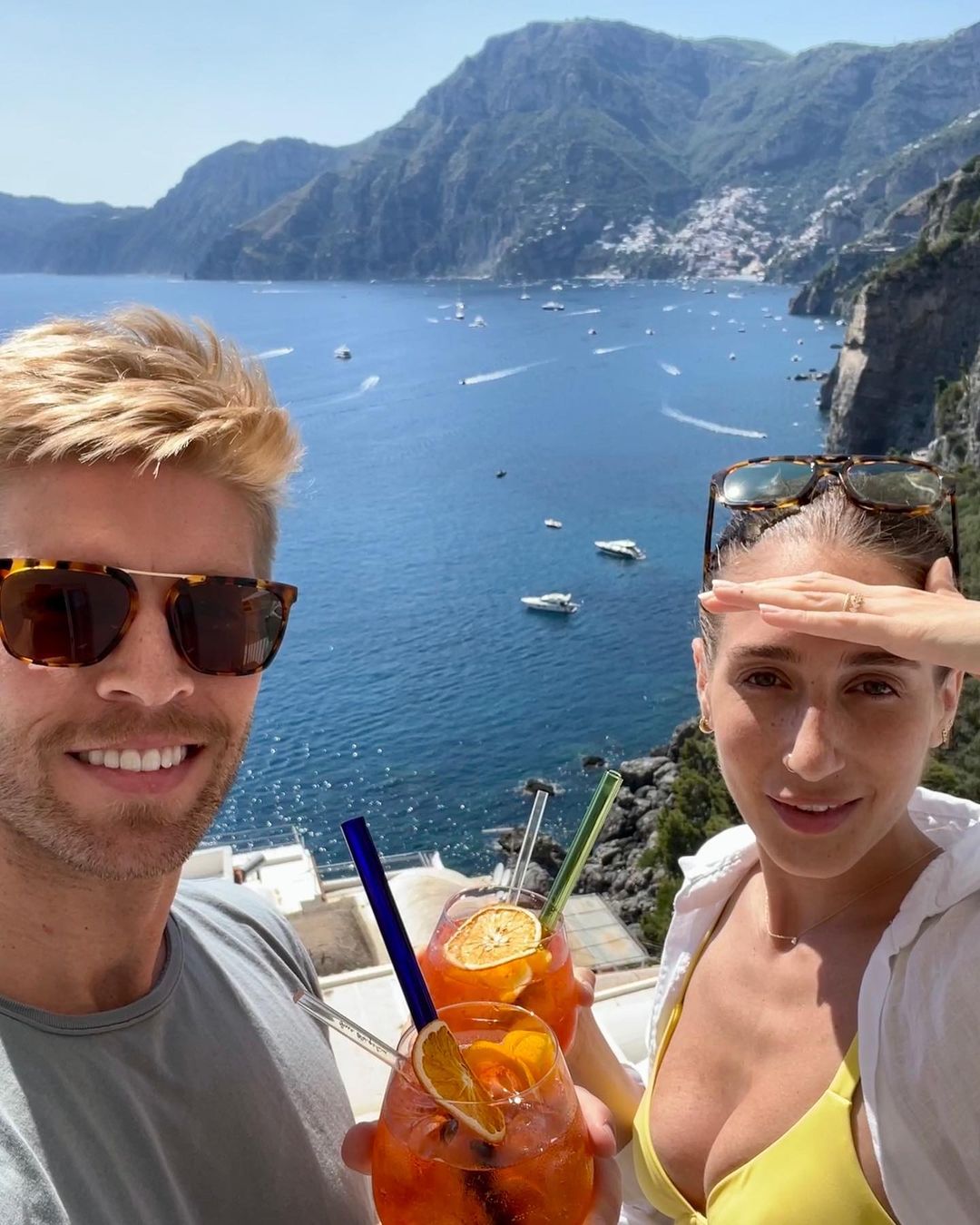 Kyle Cooke and Amanda Batula holding cocktails with a scenic view of a bay and mountains in the background.