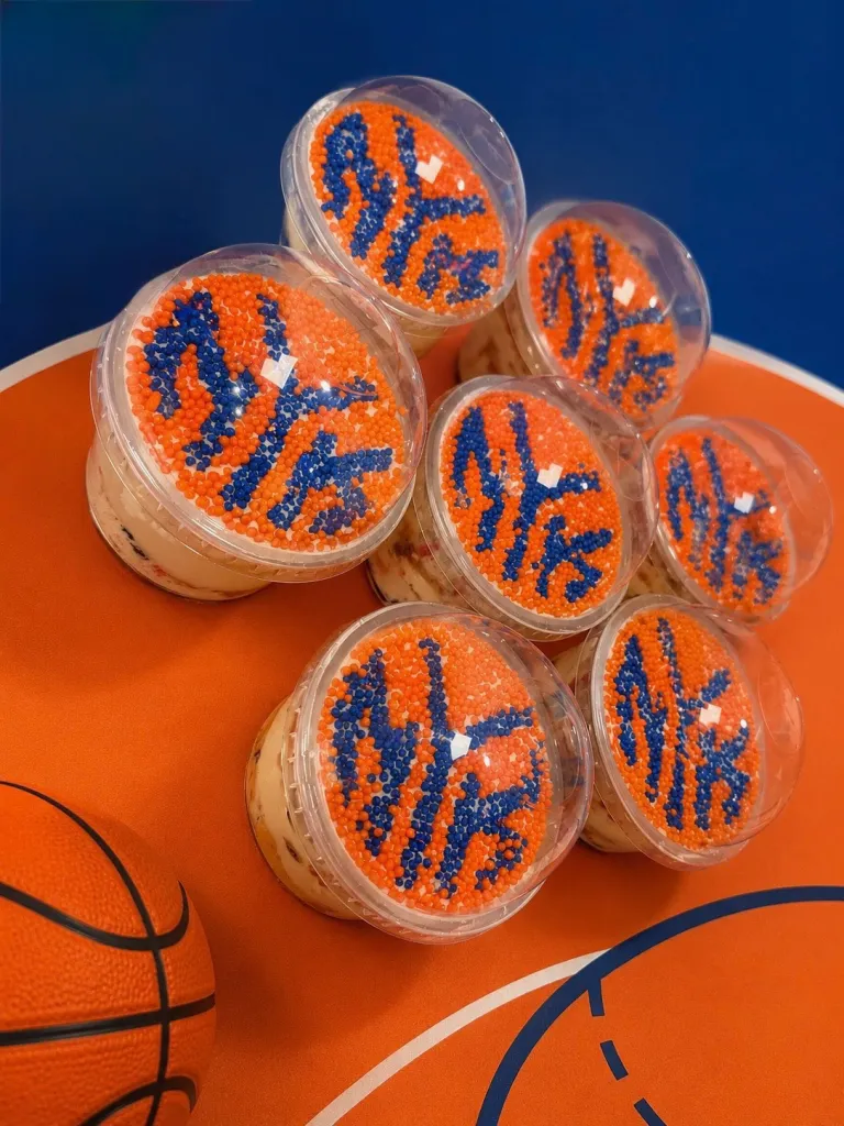 Seven dot cakes from Ladyfingers Bakery + Bar, Bloomfield, NJ, with "NYK" spelled out in blue sprinkles on an orange sprinkle background, next to a basketball.