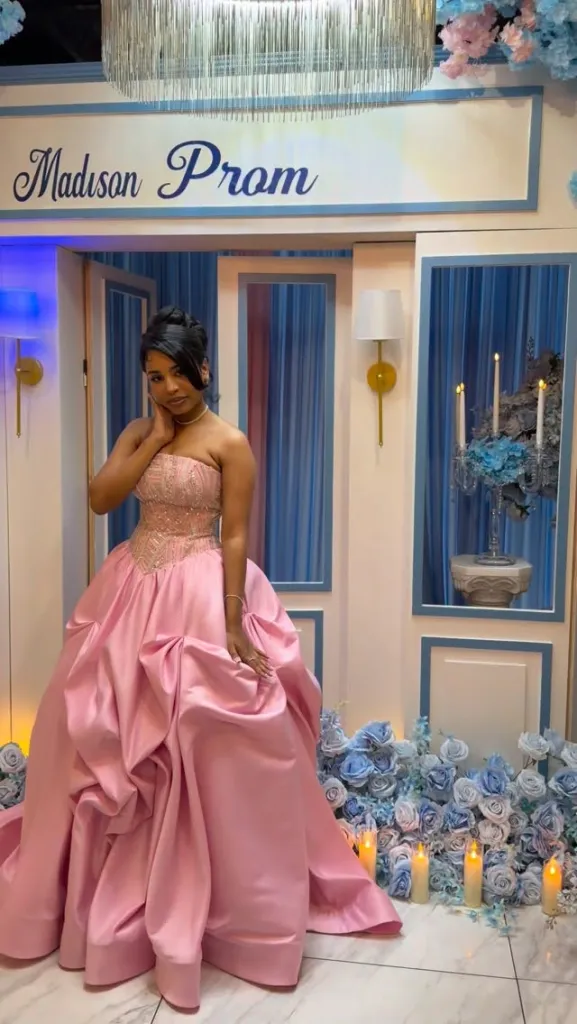 Madison Matos in a pink prom dress, standing in front of a blue and white decorated background with a sign that says "Madison Prom."