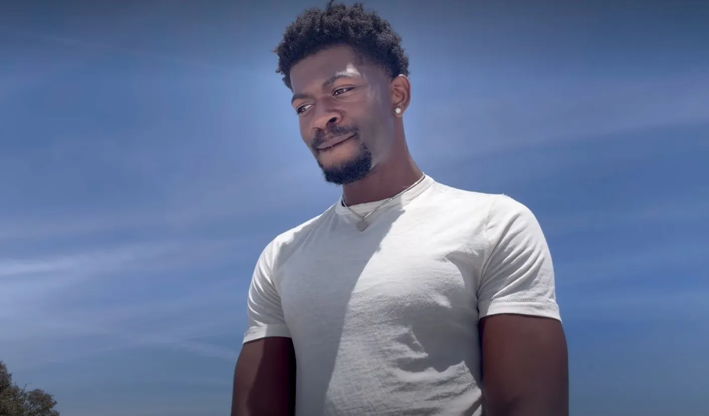 Lil Nas X looking at the camera against a blue sky.
