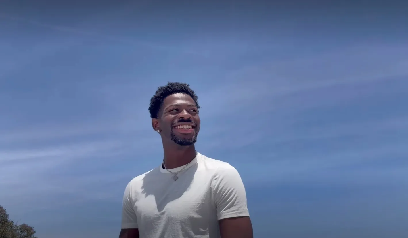 Lil Nas X smiling against a bright blue sky.