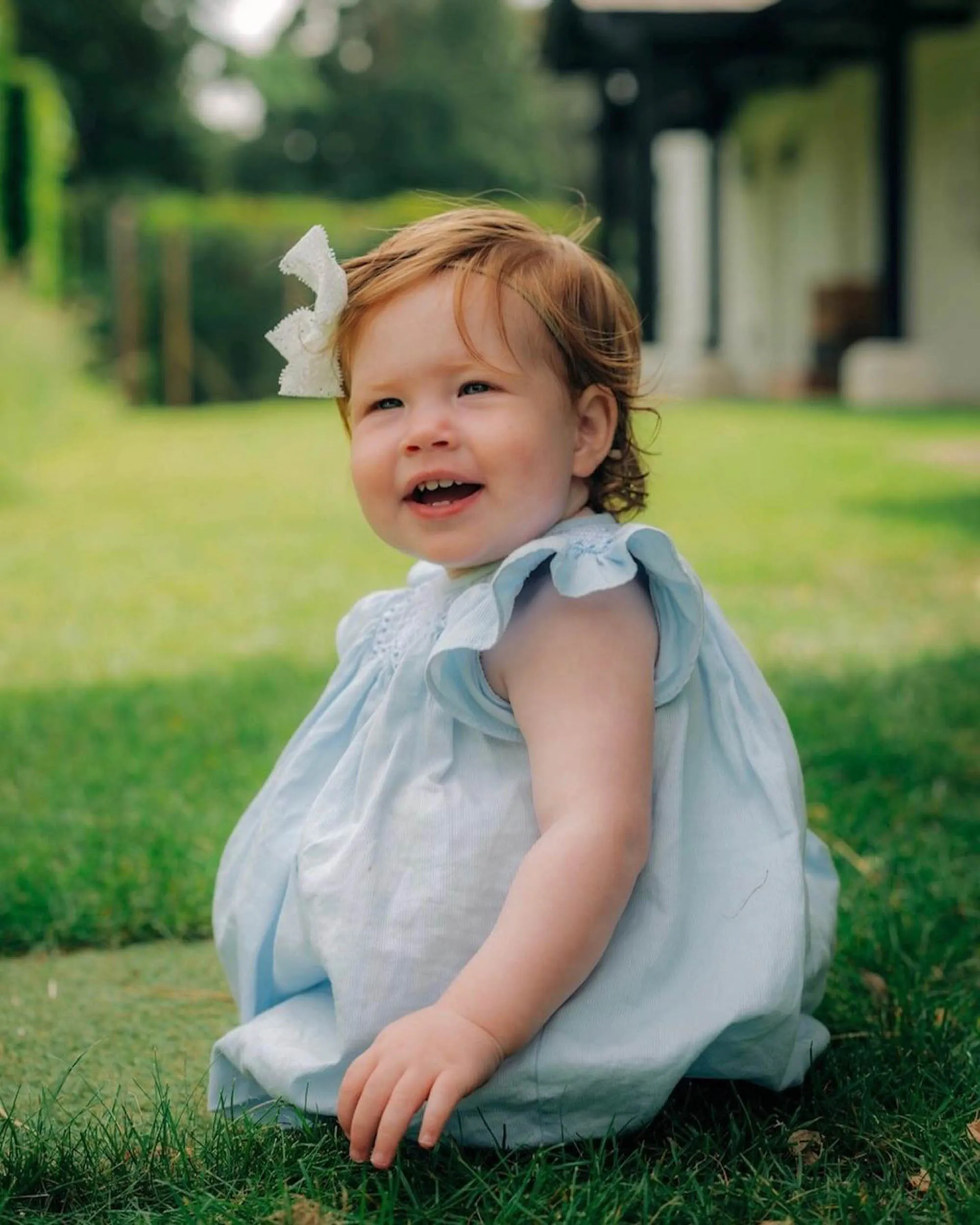 Meghan Markle holding her daughter Lilibet in the air, while Prince Harry holds their son Archie, all smiling and sitting on a wooden porch.