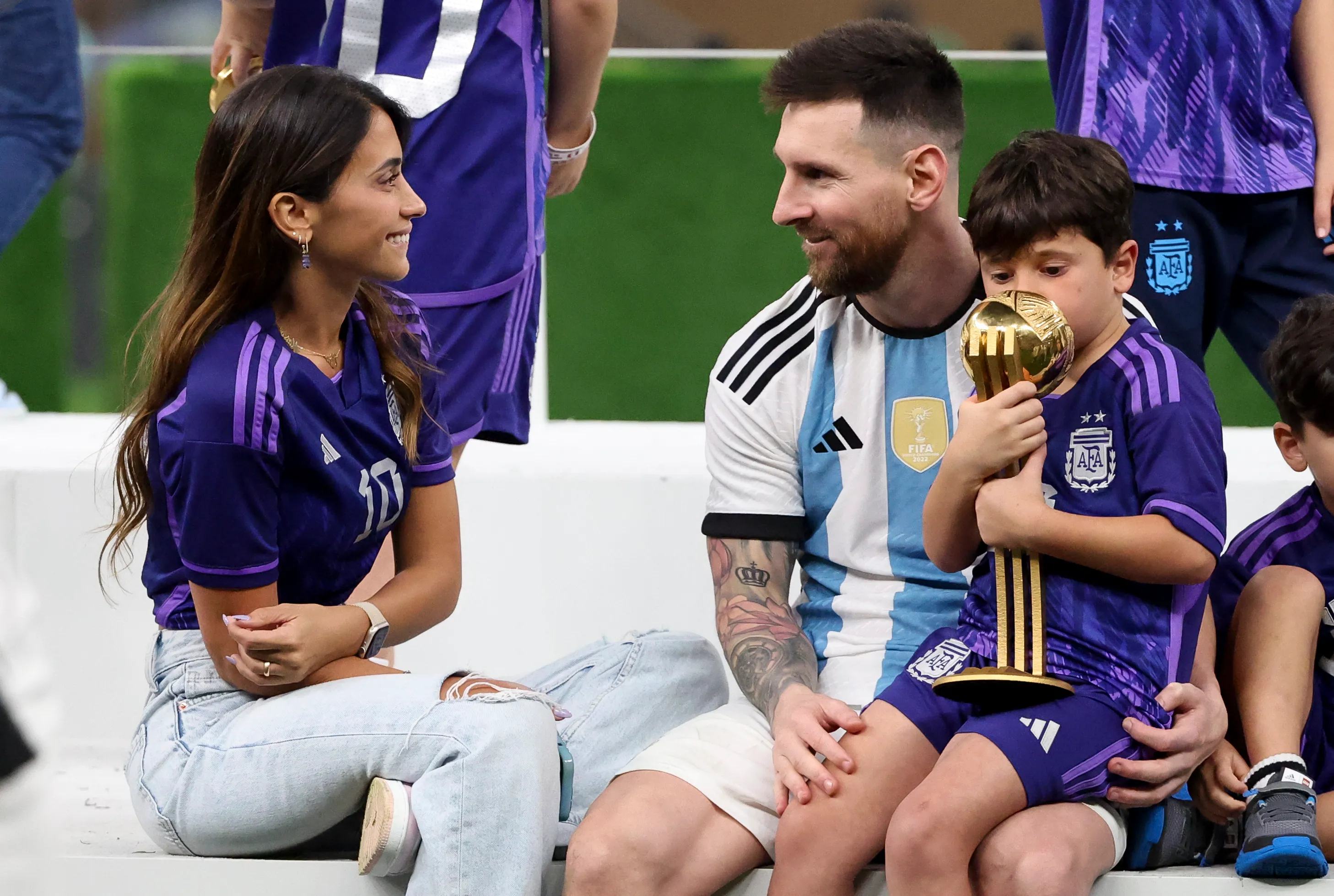 Lionel Messi with his wife Antonella Roccuzzo and their son celebrating with a trophy.