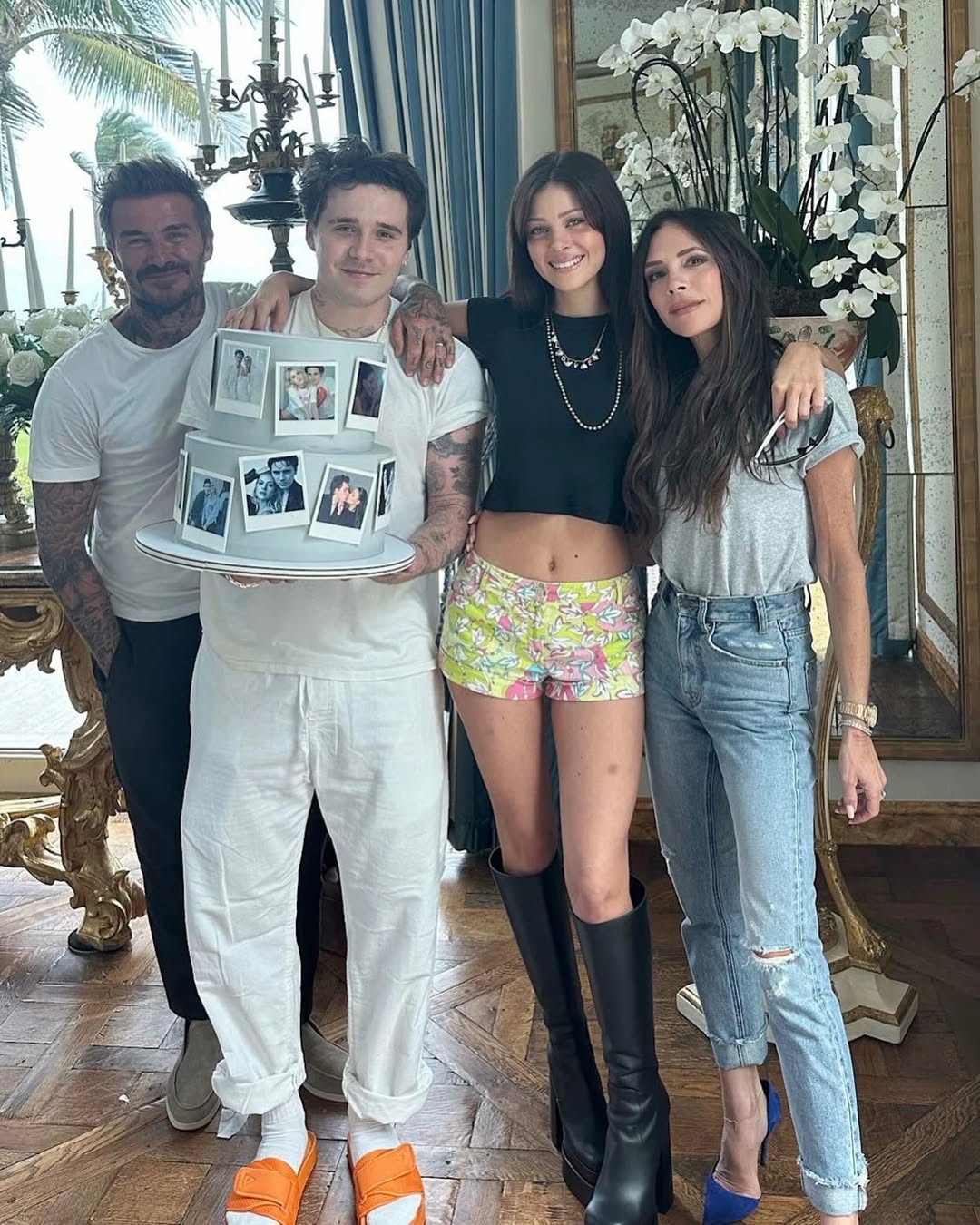 David, Victoria, Brooklyn, and Nicola Peltz Beckham pose for a photo with a cake decorated with pictures.