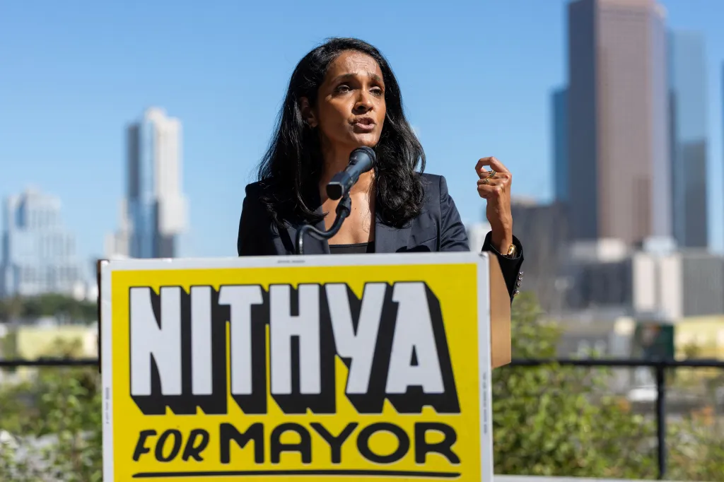 Los Angeles City Councilwoman Nithya Raman speaking at a podium with a campaign sign reading "Nithya for Mayor."