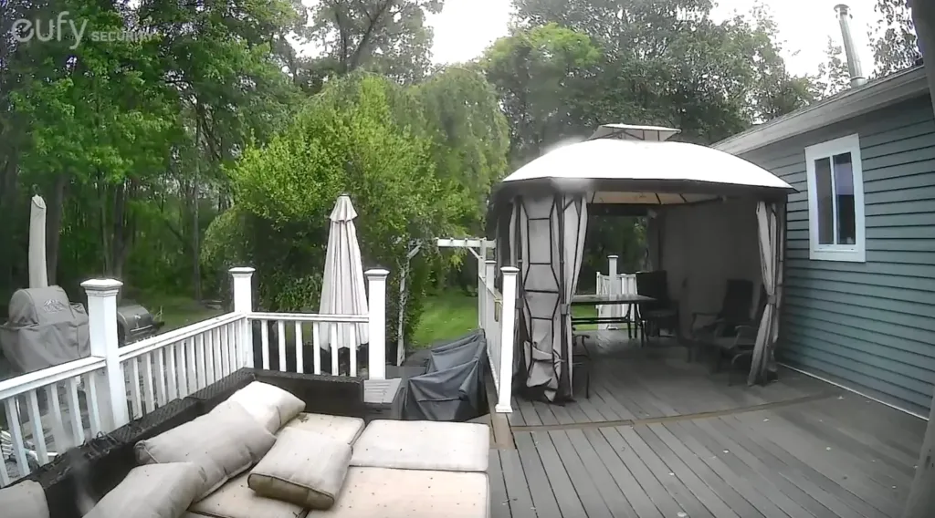 A porch with an outdoor couch, grill, and white gazebo, set against a background of lush green trees, captures the moment a meteor explodes off the coast of Massachusetts, causing a loud boom in New England.