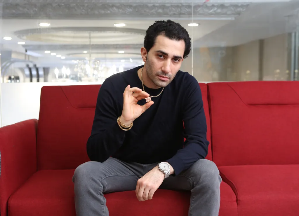 Man on red couch holding a Star of David pendant.
