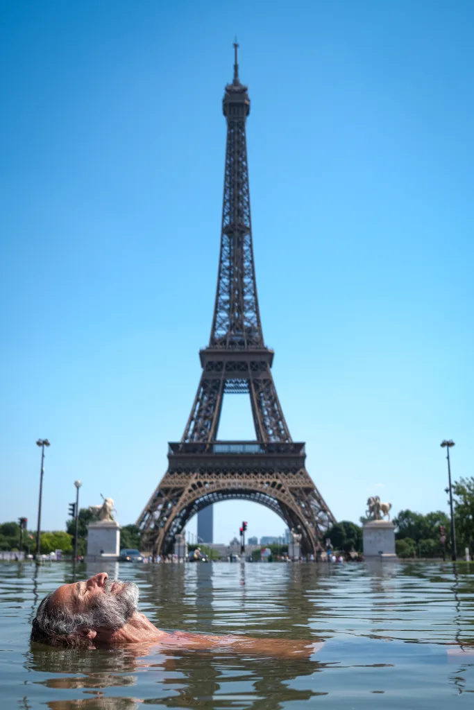 A man cools off in the Warsaw Fountain in front of the Eiffel Tower during hot weather in Paris, France.