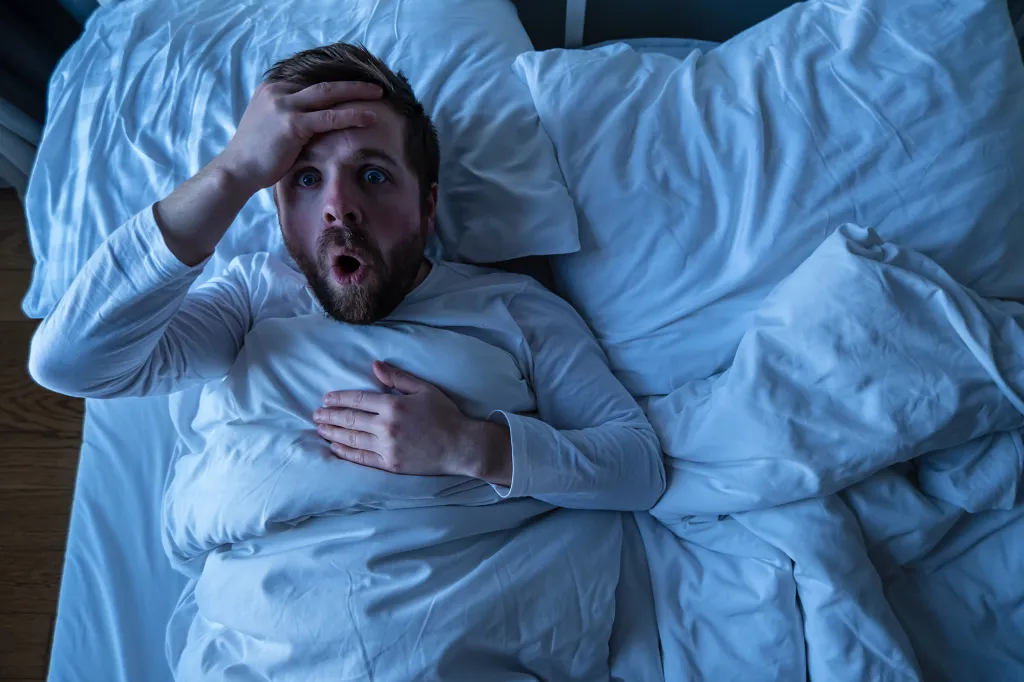 Man with wide eyes and open mouth looking scared in bed, having had a nightmare.