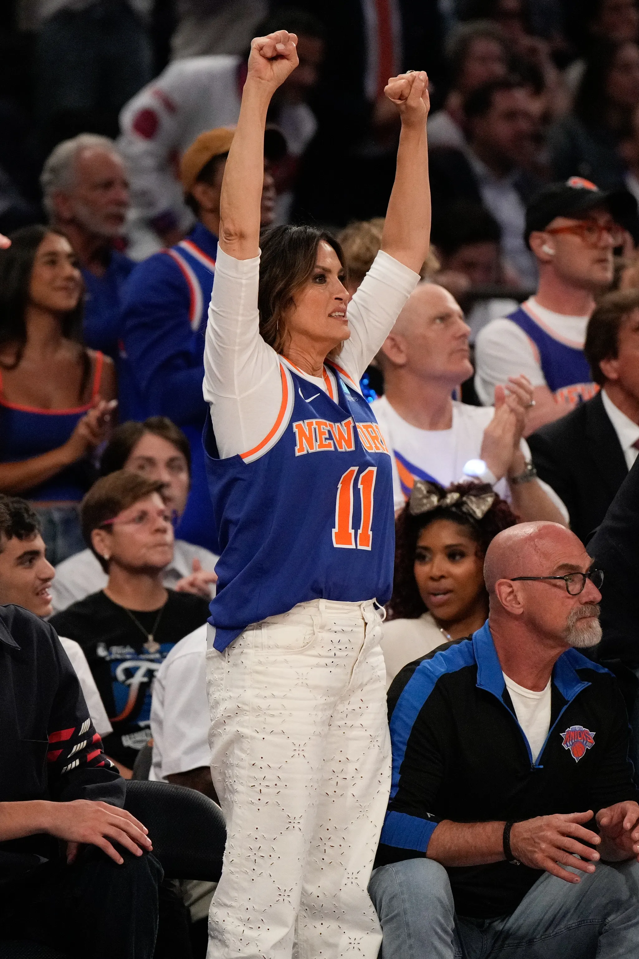 Mariska Hargitay cheering with her arms raised in a "New York" jersey at an NBA game.
