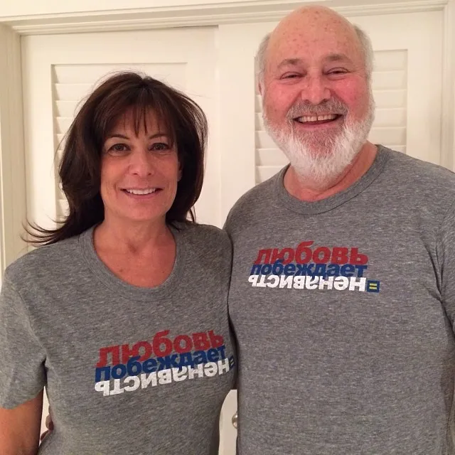 Michele and Rob Reiner smiling and wearing matching gray t-shirts with Russian text "ЛЮБОВЬ ПОБЕЖДАЕТ НЕНАВИСТЬ" ("Love Wins Over Hatred") and an equal sign.