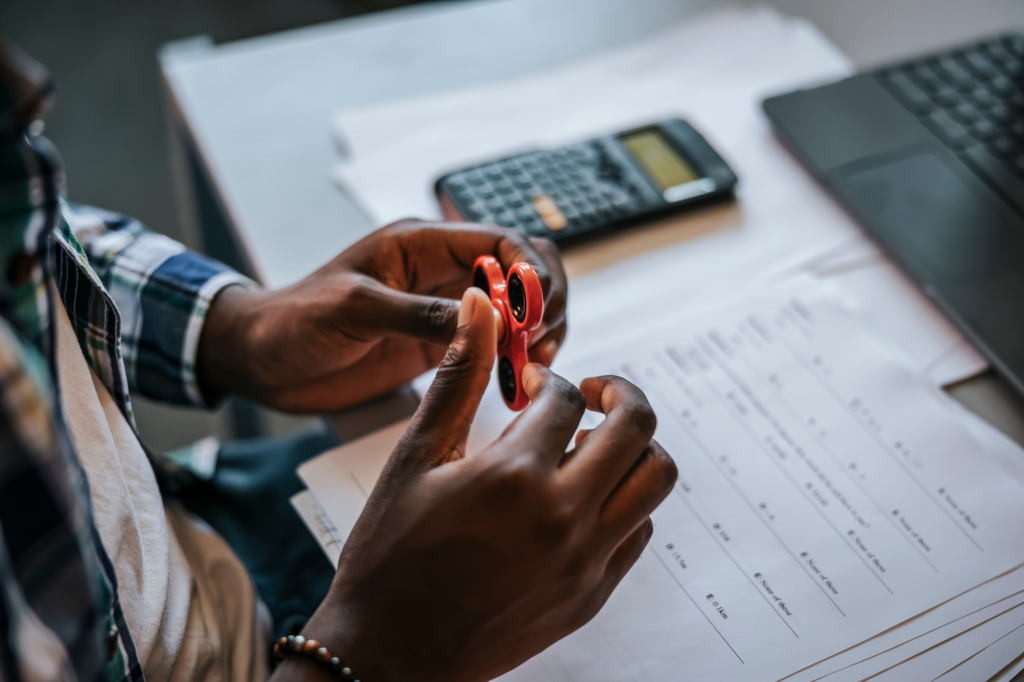 A student holding a fidget spinner, with a calculator and test papers in the background.