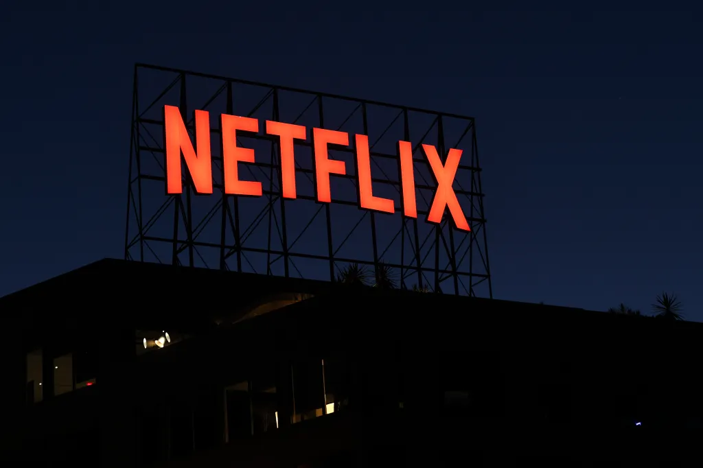 The Netflix logo illuminated in red on the roof of an office building at dusk.