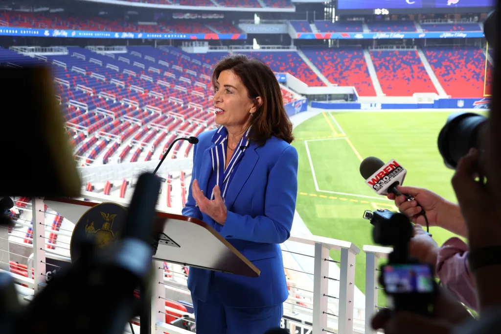 New York Gov. Kathy Hochul speaking at a podium in front of a stadium.