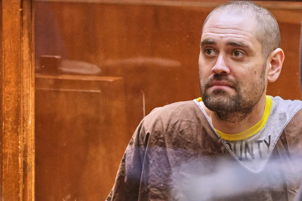 Nick Reiner in court, seen through glass, looks away from the camera.