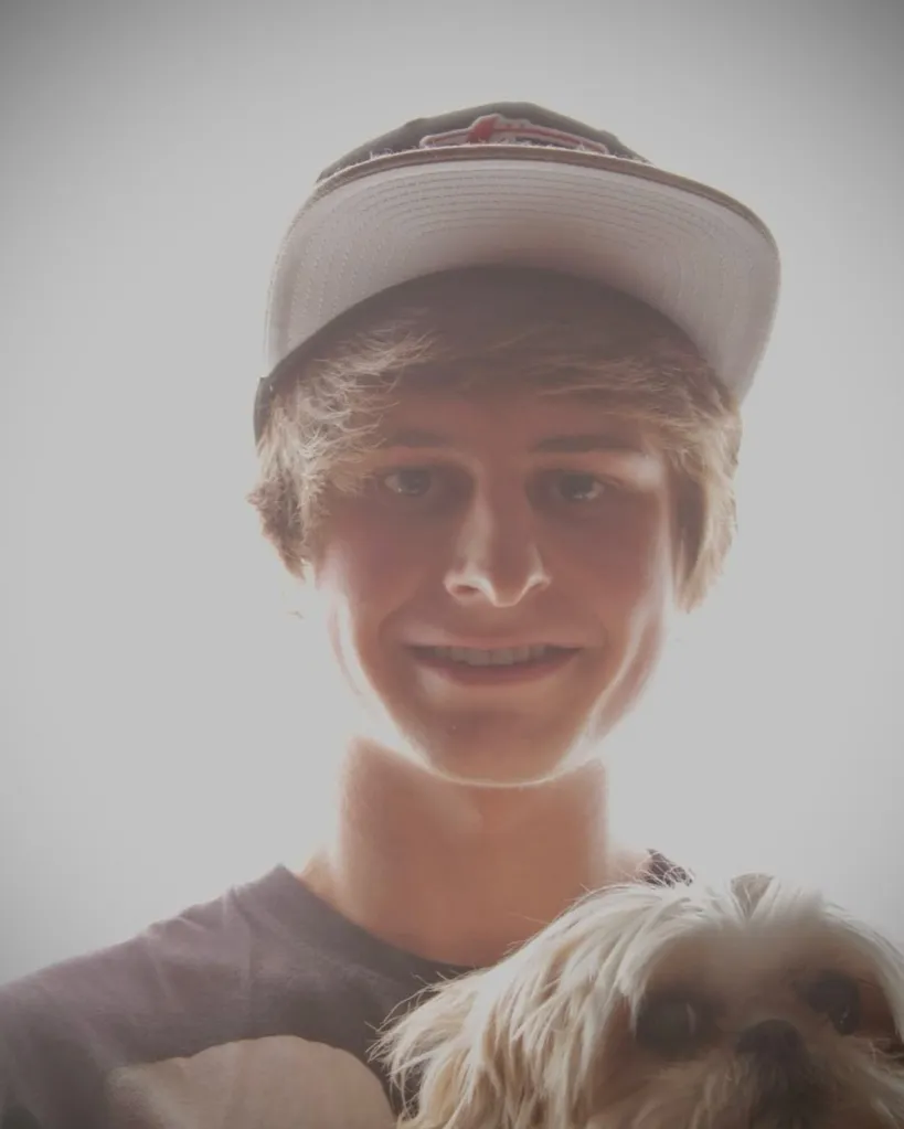 A young man in a baseball cap holding a small, fluffy dog.