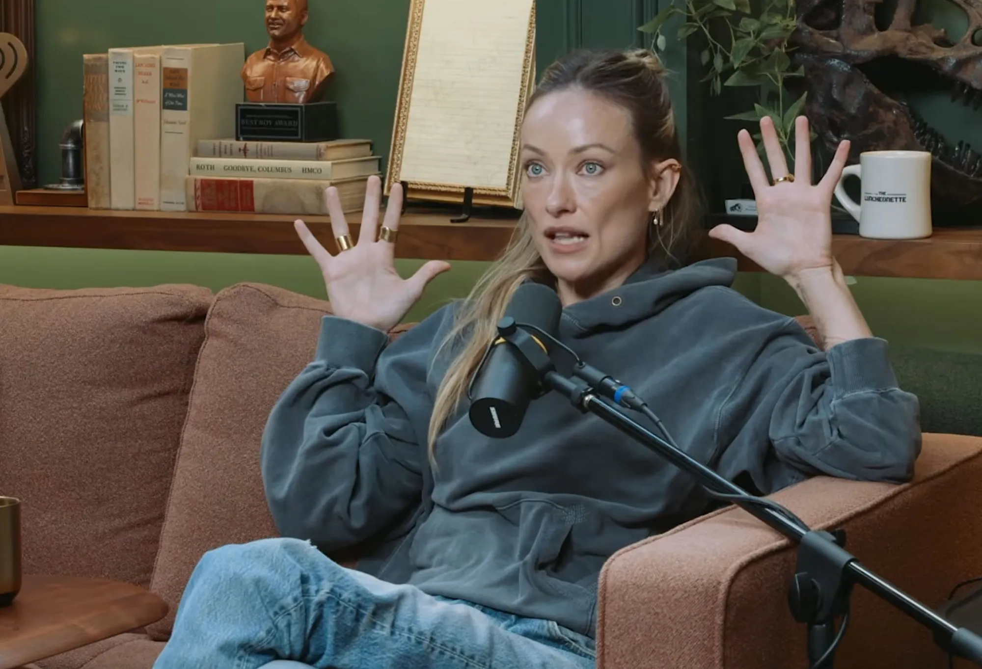 Olivia Wilde gesturing while speaking into a microphone during her "Armchair Expert" interview.