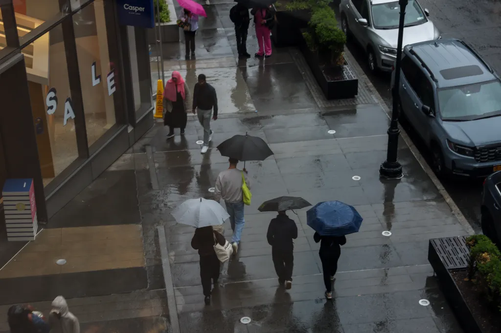 Pedestrians carrying umbrellas walk on a wet sidewalk during a rainy Memorial Day.