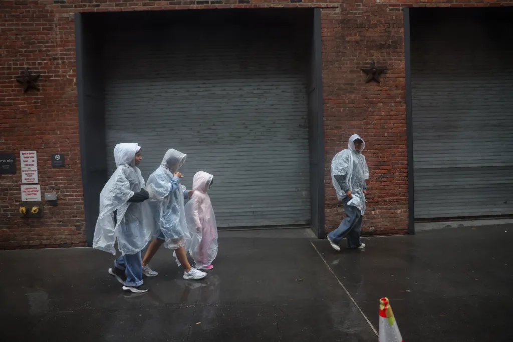 Pedestrians in rain ponchos walk on a wet sidewalk in Dumbo, Brooklyn.