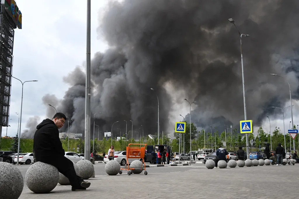 People are seen outside a shopping mall as black smoke rises from the area of the Russian oil producer Gazprom Neft's Moscow oil refinery on the south-eastern outskirts of Moscow on June 18, 2026.